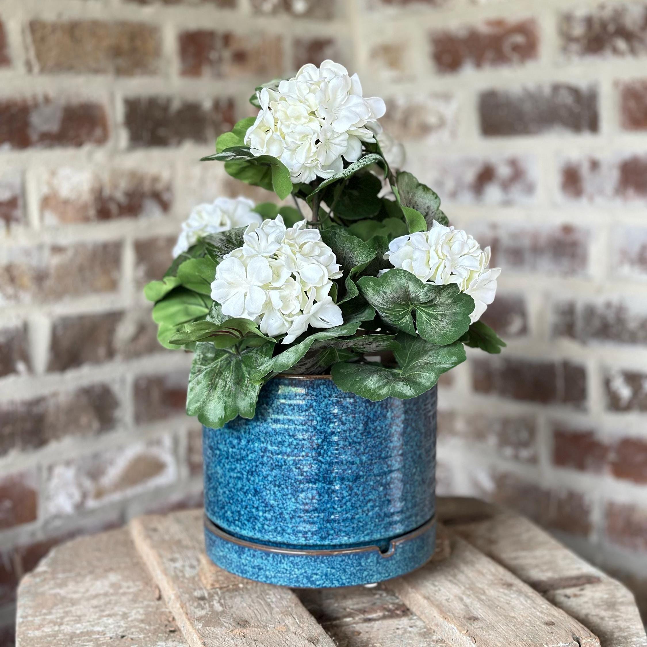 There is a 19" white geranium bush in a blue pot.  The bush has 5 blooms with artificial greenery
