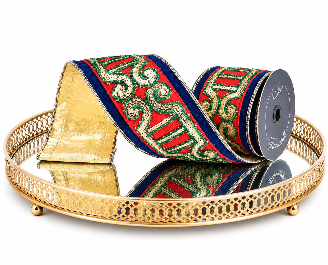 A roll of decorative ribbon with a red base, green and gold scroll pattern, and blue edges, displayed on a gold mirrored tray against a white background.